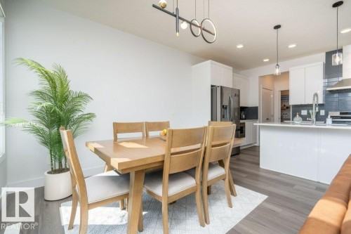 Open-concept dining area featuring wood-finish flooring, a contemporary linear chandelier, and a white baseboard trim - 5627 Kootook Place, Edmonton, AB - Indoor