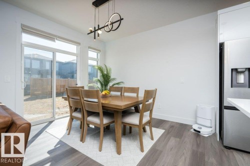 Dining area featuring wood-finish flooring, a contemporary linear chandelier, and a built-in stainless steel refrigerator - 5627 Kootook Place, Edmonton, AB - Indoor Photo Showing Dining Room