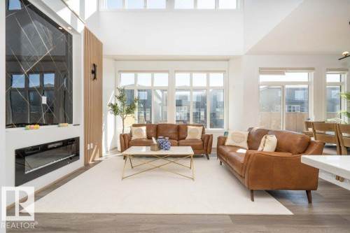 Vaulted ceiling living area featuring wood-finish flooring, an integrated linear electric fireplace with a dark paneled surround, and multiple large windows - 5627 Kootook Place, Edmonton, AB - Indoor Photo Showing Living Room With Fireplace