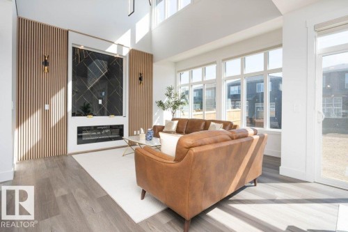 Spacious living area featuring a double-height ceiling, a floor-to-ceiling fireplace with a black patterned surround and integrated linear electric insert, and wood-finish accent paneling - 5627 Kootook Place, Edmonton, AB - Indoor Photo Showing Other Room With Fireplace
