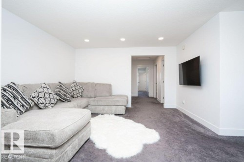 Spacious living area featuring neutral carpeting, recessed ceiling lighting, crisp white walls, and a wall-mounted television - 5627 Kootook Place, Edmonton, AB - Indoor Photo Showing Living Room