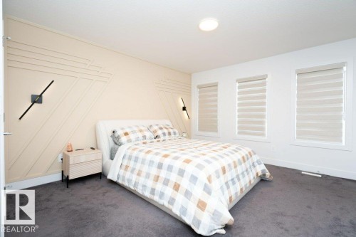 Bedroom featuring a light beige accent wall with geometric paneling, two wall-mounted sconces, and three windows equipped with layered shades - 5627 Kootook Place, Edmonton, AB - Indoor Photo Showing Bedroom