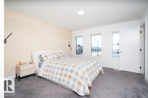 Bedroom featuring a geometric accent wall with integrated sconces, three windows, plush carpeting, and a modern interior door with brushed nickel hardware - 5627 Kootook Place, Edmonton, AB - Indoor Photo Showing Bedroom