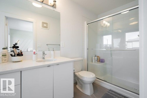 Modern bathroom featuring a single-sink vanity with a light-colored countertop, integrated mirror, and a glass-enclosed shower with sliding doors - 5627 Kootook Place, Edmonton, AB - Indoor Photo Showing Bathroom