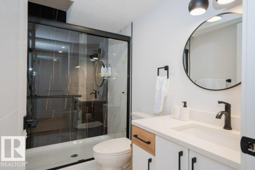 Bathroom featuring a glass-enclosed shower with black and gold veined tile, white vanity with a light-toned countertop, integrated rectangular sink, and matte black fixtures - 5627 Kootook Place, Edmonton, AB - Indoor Photo Showing Bathroom