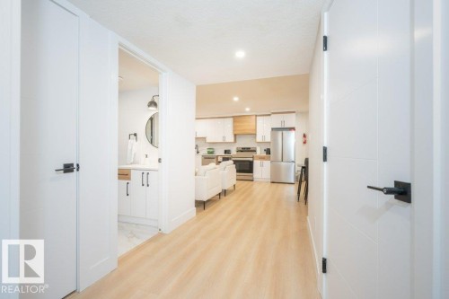 Entryway with wood-finish flooring, leading to a kitchen featuring stainless steel appliances, white cabinetry, and light wood-grain accents - 5627 Kootook Place, Edmonton, AB - Indoor