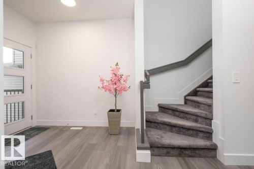 Entry foyer featuring wood-finish flooring, a white front door with three rectangular lites, and a staircase with grey carpeted treads and a matching grey handrail - 5627 Kootook Place, Edmonton, AB - Indoor Photo Showing Other Room