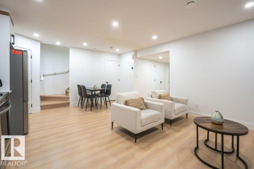 Open-concept living area featuring light wood-finish flooring, recessed ceiling lighting, a stainless steel refrigerator, and a light wood staircase with a white handrail - 5627 Kootook Place, Edmonton, AB - Indoor