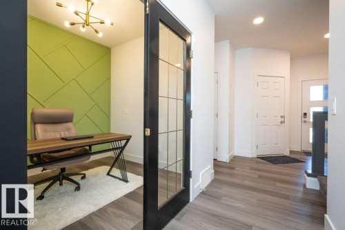 Dedicated office space with a geometric accent wall, modern brass chandelier, and a black-framed glass panel door - 5627 Kootook Place, Edmonton, AB - Indoor Photo Showing Other Room