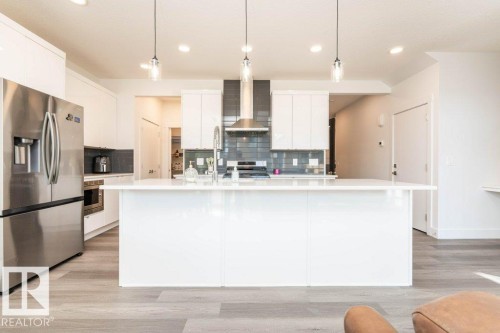 Spacious kitchen featuring a large central island with a white countertop, stainless steel appliances, white cabinetry, a gray tiled backsplash, and recessed lighting - 5627 Kootook Place, Edmonton, AB - Indoor Photo Showing Kitchen With Upgraded Kitchen