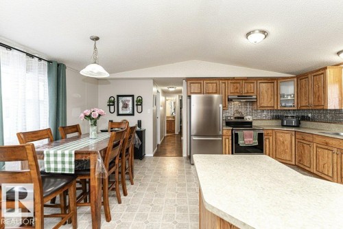 Open concept kitchen and dining area featuring wood cabinetry, stainless steel appliances, a kitchen island with ample counter space, and durable linoleum flooring - 1637 68 Avenue, Edmonton, AB - Indoor