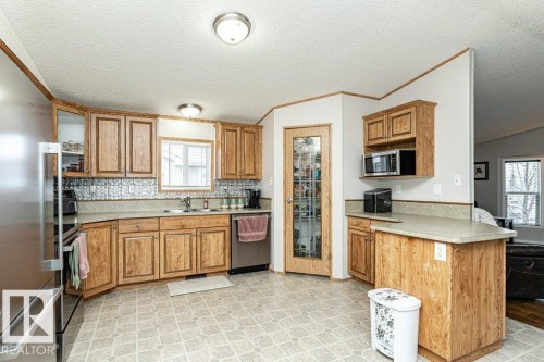 Spacious kitchen featuring wood cabinetry, stainless steel appliances, patterned backsplash, a corner sink with window, and a frosted glass pantry door - 1637 68 Avenue, Edmonton, AB - Indoor Photo Showing Kitchen