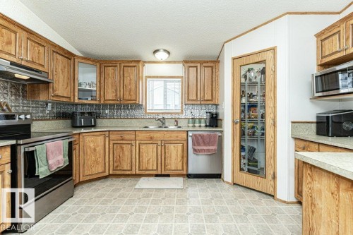 Kitchen featuring warm wood-finish cabinetry, a patterned tile backsplash, and light-toned countertops - 1637 68 Avenue, Edmonton, AB - Indoor Photo Showing Kitchen With Double Sink