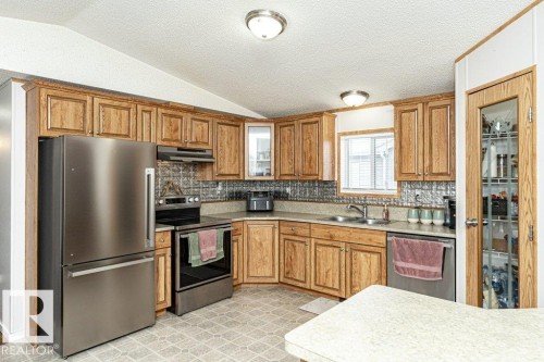 Kitchen featuring wood-finish cabinetry, stainless steel appliances, a textured backsplash, and a double basin sink - 1637 68 Avenue, Edmonton, AB - Indoor Photo Showing Kitchen With Stainless Steel Kitchen With Double Sink