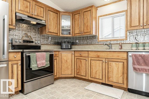 Kitchen featuring wood cabinetry, stainless steel appliances, a tin-style backsplash, and a window above the sink - 1637 68 Avenue, Edmonton, AB - Indoor Photo Showing Kitchen With Stainless Steel Kitchen