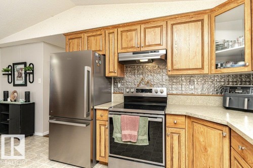 Kitchen featuring wood cabinetry, stainless steel appliances, a textured backsplash, and light-toned countertops - 1637 68 Avenue, Edmonton, AB - Indoor Photo Showing Kitchen With Stainless Steel Kitchen