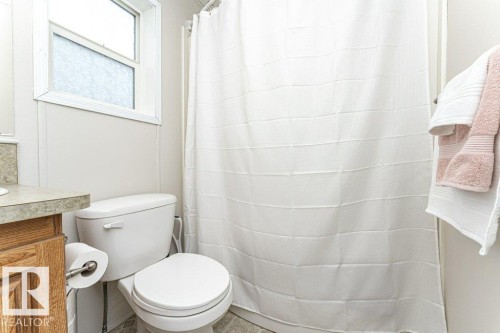 Bathroom featuring a white toilet, wood-finish vanity, and a shower with a white curtain - 1637 68 Avenue, Edmonton, AB - Indoor Photo Showing Bathroom