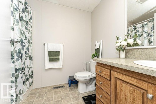 Bathroom featuring a wood-finish vanity with a laminate countertop, an integrated sink, and a large wall-mounted mirror - 1637 68 Avenue, Edmonton, AB - Indoor Photo Showing Bathroom