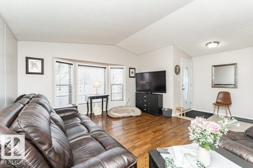 Living area featuring wood-finish flooring, a bay window with blinds, and white wall paneling - 1637 68 Avenue, Edmonton, AB - Indoor Photo Showing Living Room