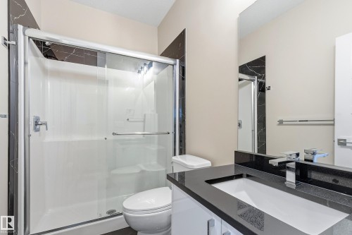Modern bathroom featuring a glass-enclosed shower with a white surround, a sleek vanity with a black countertop and integrated sink, a contemporary chrome faucet, and a large wall mirror - 3714 40 Avenue, Beaumont, AB - Indoor Photo Showing Bathroom