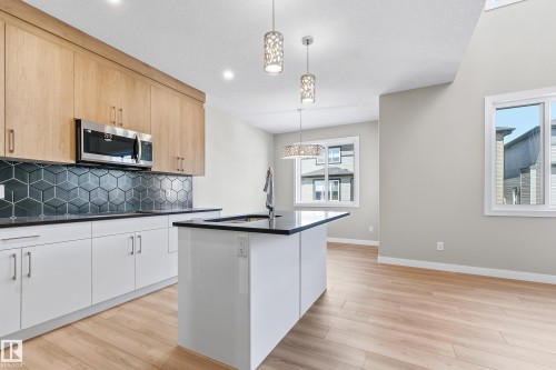 Modern kitchen featuring wood-finish upper cabinetry, white lower cabinetry, and a geometric tile backsplash - 3714 40 Avenue, Beaumont, AB - Indoor Photo Showing Kitchen