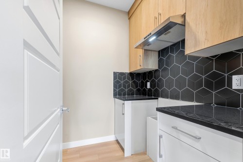 Modern kitchen area featuring light wood-finish upper cabinetry, white lower cabinetry with stainless steel pull hardware, and black countertops - 3714 40 Avenue, Beaumont, AB - Indoor Photo Showing Kitchen