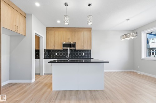 Modern kitchen featuring a central island with a dark countertop, light wood-finish cabinetry, and a black hexagonal tile backsplash - 3714 40 Avenue, Beaumont, AB - Indoor Photo Showing Kitchen With Double Sink