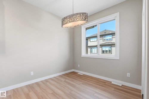 Spacious room featuring wood-finish flooring, light grey painted walls, white baseboards, and a contemporary chandelier - 3714 40 Avenue, Beaumont, AB - Indoor Photo Showing Other Room