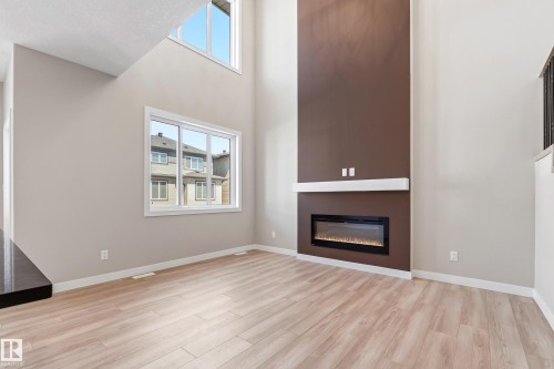 Living area featuring a floor-to-ceiling accent wall with a linear electric fireplace, wood-finish flooring, and high ceilings with upper-level windows - 3714 40 Avenue, Beaumont, AB - Indoor Photo Showing Living Room With Fireplace