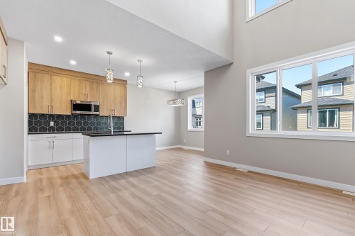 Open-concept living space featuring wood-finish flooring, a kitchen island with a black countertop, and a two-story window wall - 3714 40 Avenue, Beaumont, AB - Indoor Photo Showing Kitchen With Upgraded Kitchen