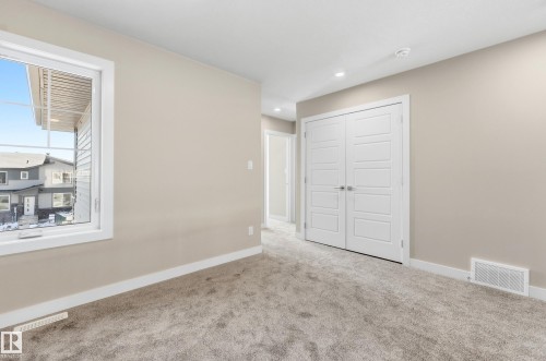 Spacious room featuring neutral wall paint, plush carpet flooring, a large window with white trim, and a double-door closet with contemporary paneling - 3714 40 Avenue, Beaumont, AB - Indoor Photo Showing Other Room