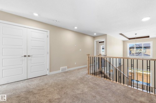 Carpeted upper-level landing featuring a contemporary chandelier, recessed ceiling lighting, a window with exterior views, and a staircase with light wood handrails and black metal balusters - 3714 40 Avenue, Beaumont, AB - Indoor Photo Showing Other Room