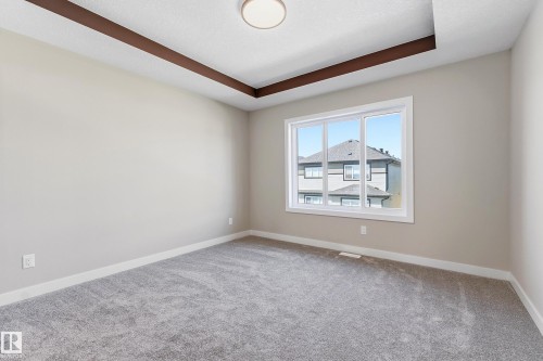 Spacious room featuring a tray ceiling with dark wood-finish accents, a large multi-pane window, neutral-toned walls, plush gray carpeting, and white baseboards - 3714 40 Avenue, Beaumont, AB - Indoor Photo Showing Other Room