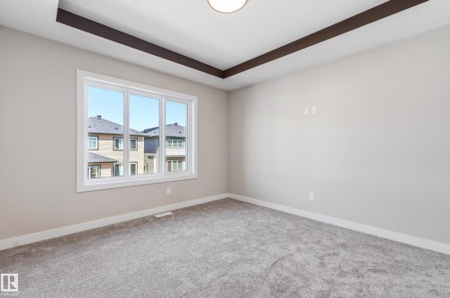 Spacious interior room featuring light gray carpeting, neutral wall paint, white trim, and a tray ceiling with dark accent beams - 3714 40 Avenue, Beaumont, AB - Indoor Photo Showing Other Room