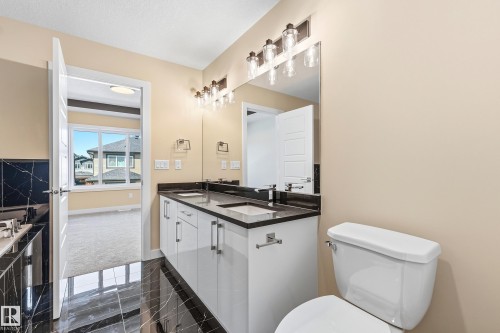Bathroom featuring a dual vanity with undermount sinks, dark countertops, and white cabinetry - 3714 40 Avenue, Beaumont, AB - Indoor Photo Showing Bathroom