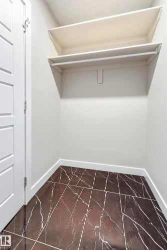 Walk-in closet with dark marble-look tile flooring, white baseboards, and two built-in shelves with a hanging rod - 3714 40 Avenue, Beaumont, AB - Indoor With Storage