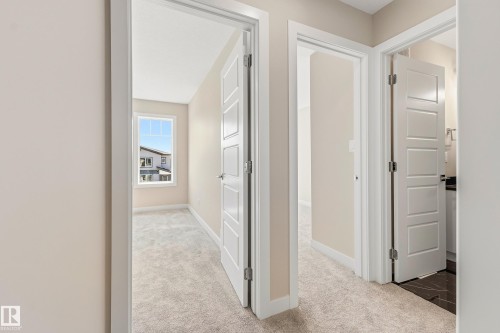 Hallway with light beige carpeting and white trim, featuring two panel-style doors and a rectangular window - 3714 40 Avenue, Beaumont, AB - Indoor Photo Showing Other Room
