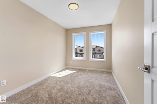 Neutral-toned interior room featuring twin windows, plush carpeting, a flusht mount ceiling light, and a white paneled door with brushed nickel hardware - 3714 40 Avenue, Beaumont, AB - Indoor Photo Showing Other Room
