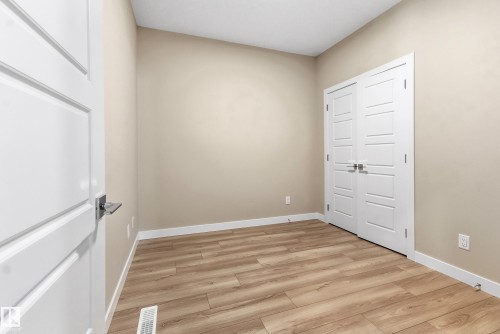 Neutral wall paint with white trim, wood-finish flooring, and white paneled double closet doors - 3714 40 Avenue, Beaumont, AB - Indoor Photo Showing Other Room