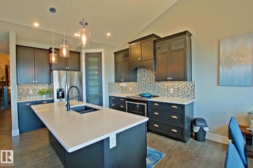 Kitchen featuring dark cabinetry, white countertops, stainless steel appliances, wood-finish flooring, and a patterned tile backsplash - 9711 223 Street, Edmonton, AB 