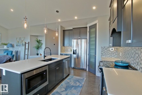 Gourmet kitchen featuring a large island with sink, stainless steel appliances, dark cabinetry, and a mosaic tile backsplash - 9711 223 Street, Edmonton, AB 