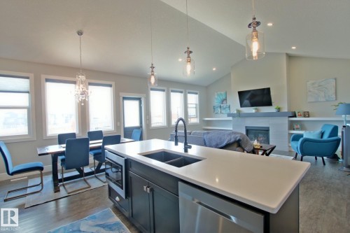 Open-concept living area featuring a kitchen island with dual sinks and built-in microwave, wood-finish flooring, vaulted ceilings, and a fireplace with integrated shelving - 9711 223 Street, Edmonton, AB 