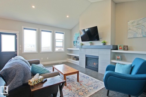 Living area featuring a vaulted ceiling, recessed lighting, three large windows, a fireplace with a light-toned tile surround and dark mantel, and built-in shelving - 9711 223 Street, Edmonton, AB 