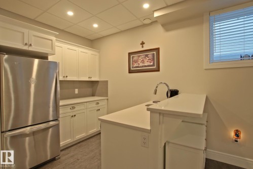 Kitchenette featuring white shaker-style cabinetry, a stainless steel refrigerator, and light-toned countertops - 9711 223 Street, Edmonton, AB 