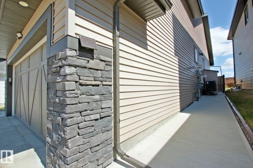 Contemporary exterior featuring a panel-style garage door, stacked stone accent column, horizontal siding, and a concrete walkway - 9711 223 Street, Edmonton, AB 