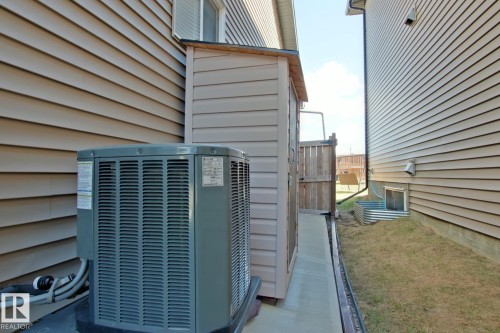 Exterior siding with a window, featuring an air conditioning unit, a compact storage shed, a wooden fence gate, and a basement window well - 9711 223 Street, Edmonton, AB 