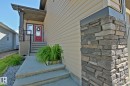 Exterior entry featuring a red door with decorative glass inserts, stone accents on the columns, and concrete steps - 9711 223 Street, Edmonton, AB 