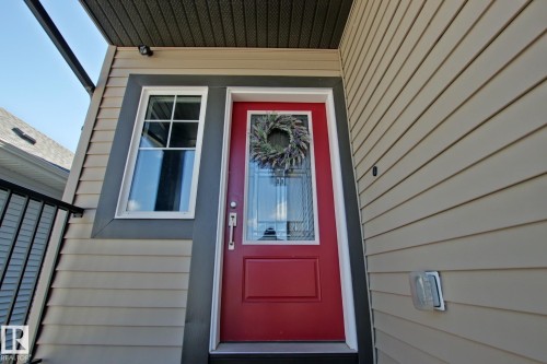Vibrant red entry door with glass paneling and a white frame, complemented by light beige siding - 9711 223 Street, Edmonton, AB 