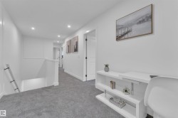 Bright hallway featuring recessed lighting, a built-in white desk with shelving, light gray carpeting, crisp white walls, and dark hardware on interior doors - 