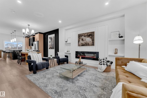 Open-concept living space featuring wood-finish flooring, a contemporary fireplace within a paneled feature wall with integrated shelving, and recessed lighting throughout - 269 Falcon Crescent, Leduc, AB - Indoor Photo Showing Living Room With Fireplace